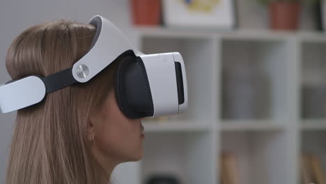 female-teenager-is-using-HMD-display-in-home-moving-hands-for-controlling-modern-technology-of-video-games-closeup-portrait-indoor